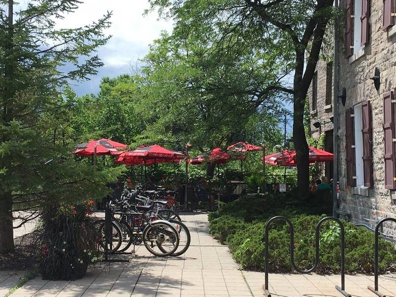 Bicycles are parked underneath umbrellas near a patio. On the right is part of an historic building visible.